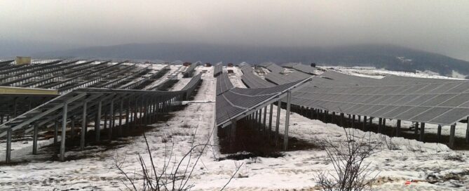 Planta de paneles solares fotovoltaicos instalados en un terreno nevado con montañas al fondo