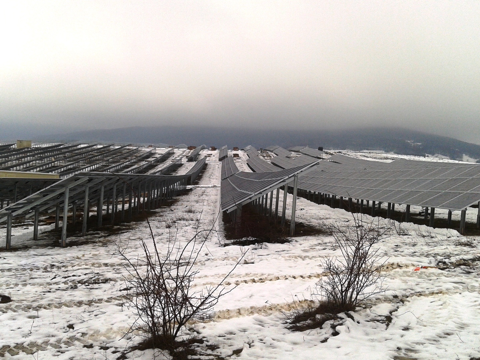 Planta de paneles solares fotovoltaicos instalados en un terreno nevado con montañas al fondo