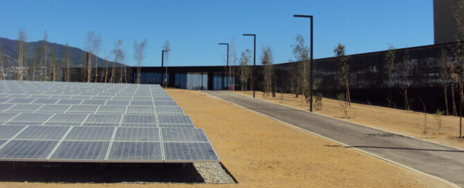 Paneles solares fotovoltaicos instalados en complejo empresarial moderno con camino asfaltado y farolas, energía renovable y arquitectura sostenible