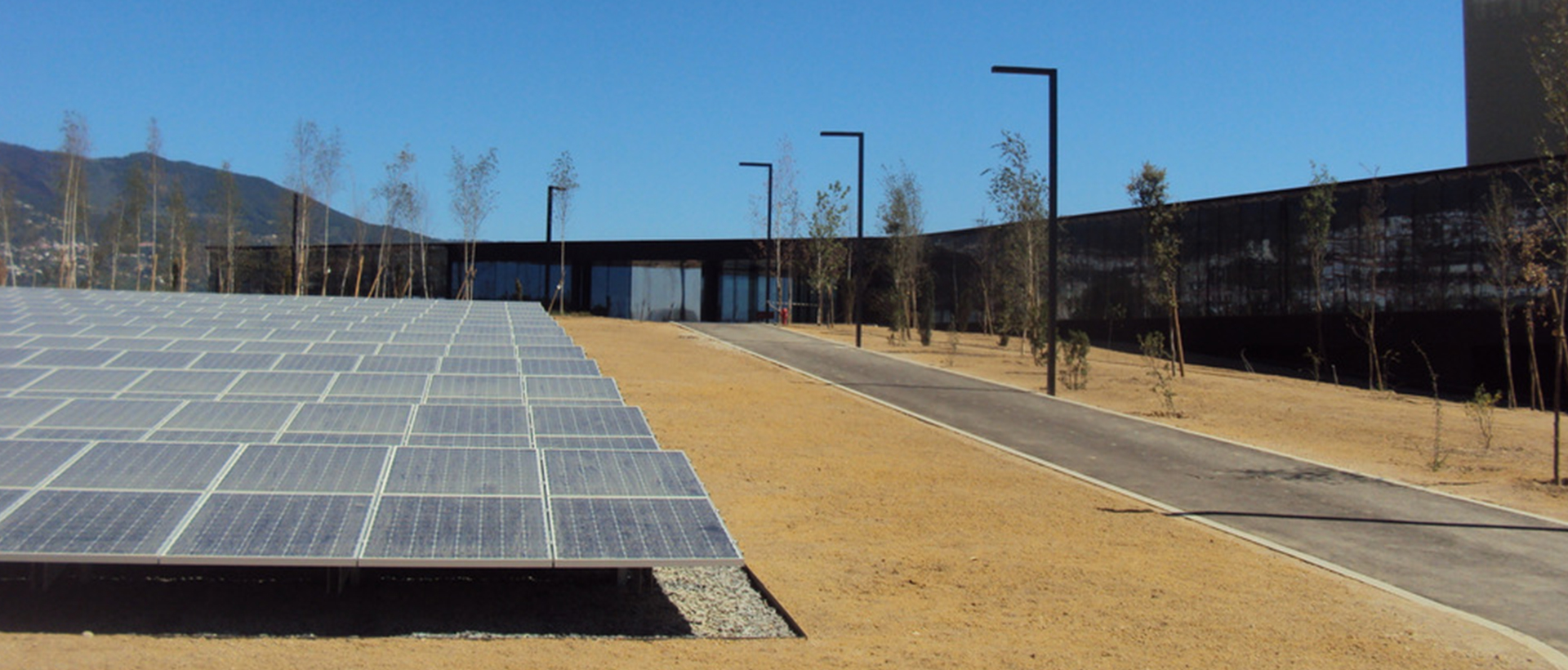 Paneles solares fotovoltaicos instalados en complejo empresarial moderno con camino asfaltado y farolas, energía renovable y arquitectura sostenible