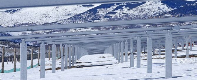 Estructuras metálicas para paneles solares instaladas en un campo nevado con montañas al fondo