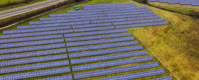 Campo de paneles solares fotovoltaicos instalados en un terreno verde junto a una carretera