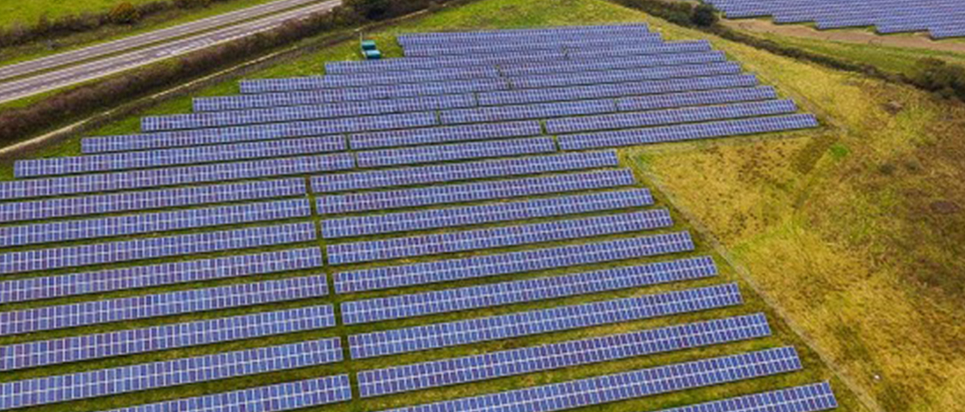 Campo de paneles solares fotovoltaicos instalados en un terreno verde junto a una carretera
