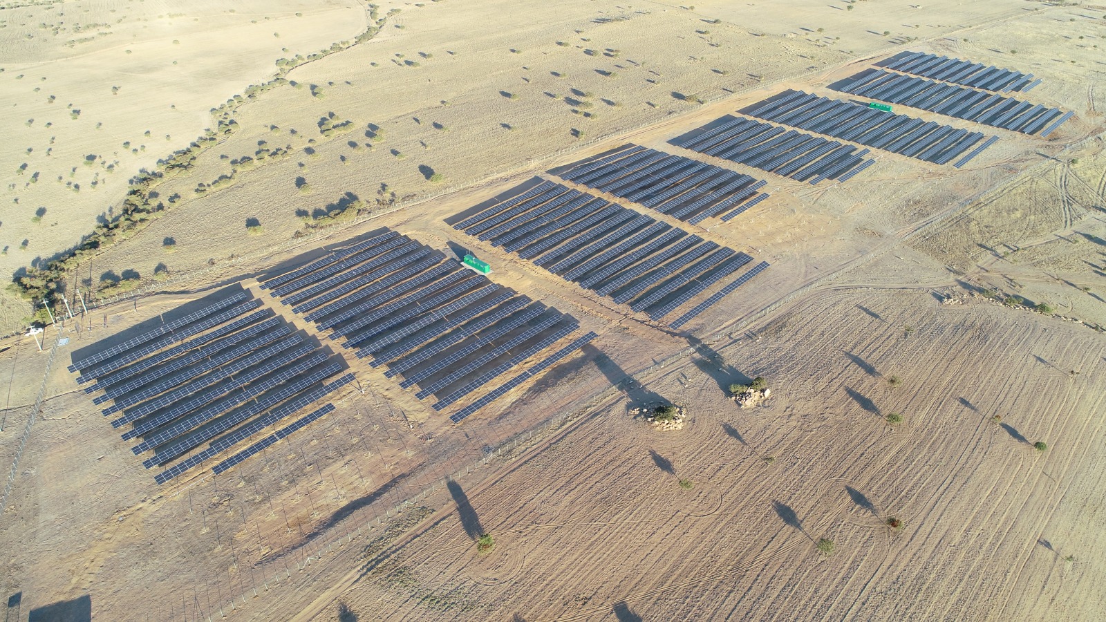 Planta solar fotovoltaica en medio del desierto con dunas de arena y montañas al fondo
