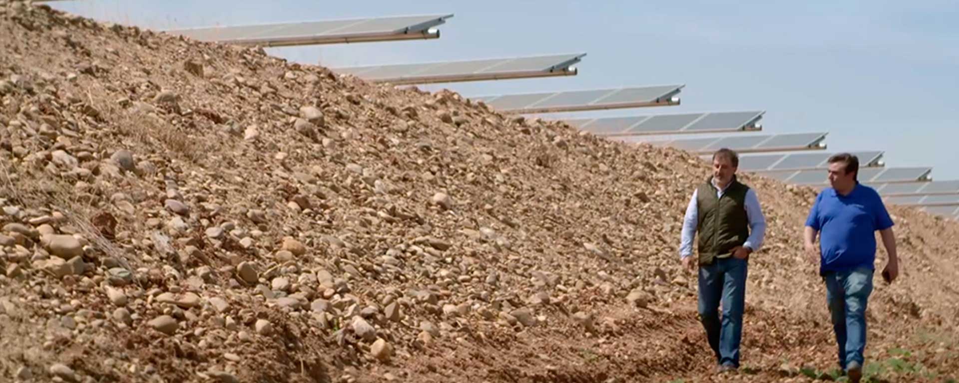 Placas solares instaladas en superficie sin construcciones y dos personas encargadas caminando a un lado